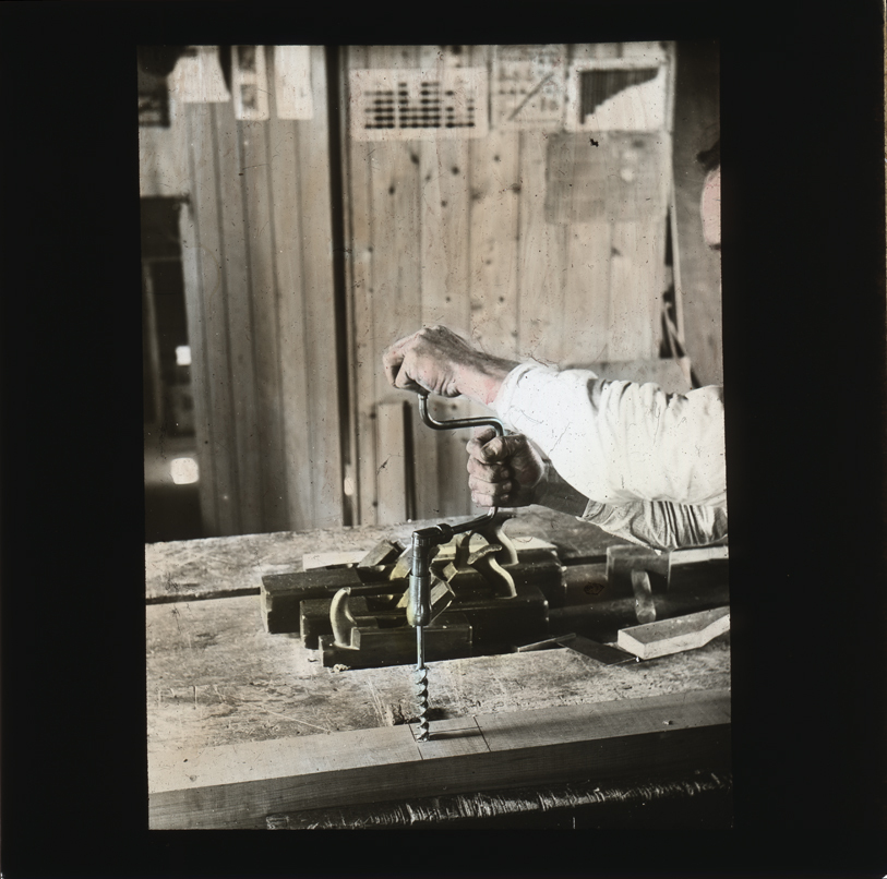 Woodworking - hands holding and using a bit and brace for cutting holes. Wooden hand block planes in background [Hawkesbury Agricultural College (HAC)]