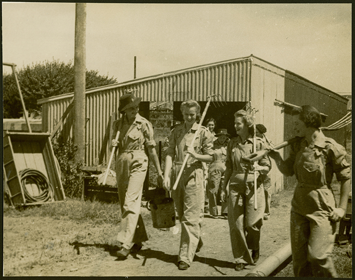 Women's Land Army: Women dressed in overalls and carrying rakes and forks setting off to work in the fields [Hawkesbury Agricultural College (HAC)]