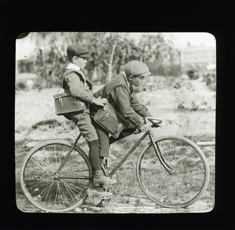 Two school boys on a bicycle. Slide titled 'Giving a lift to a Schoolmate' [Hawkesbury Agricultural College (HAC)]