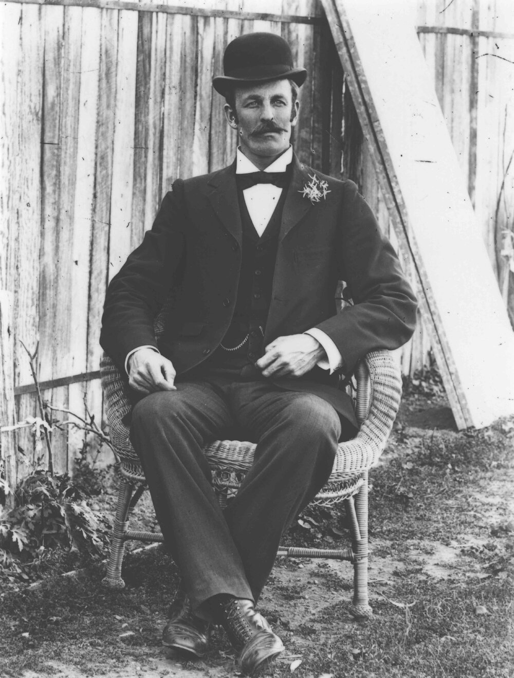 Portrait: Man, formally dressed in suit and waistcoat, wearing a bowler hat and seated in a cane chair [Hawkesbury Agricultural College (HAC)]