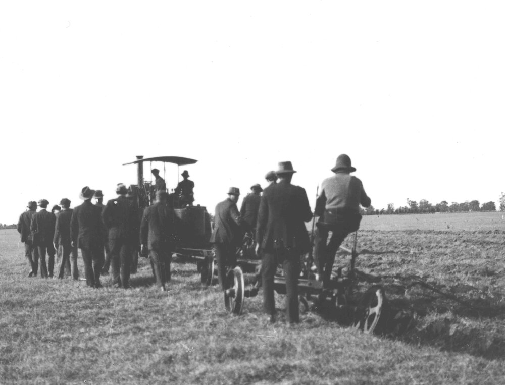 Tractor drawing a plough - A group of farmers watching and walking alongside the demonstration [Hawkesbury Agricultural College (HAC)]