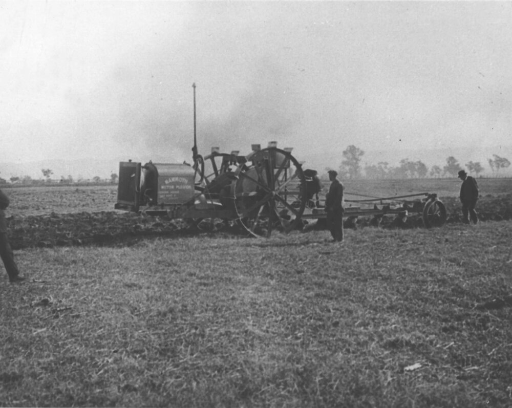 Very early model tractor pulling a plough, men inspecting its progress - 'Mammoth Motor Plough' written on the side of the machine [Hawkesbury Agricultural College (HAC)]