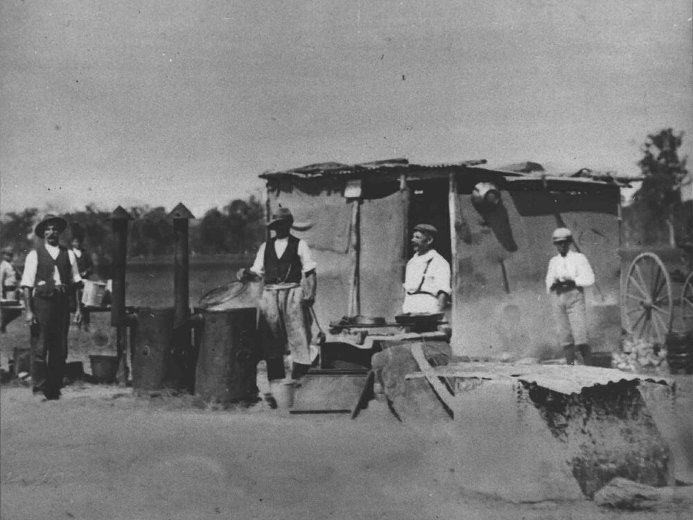 Land clearing - men standing outside a shack, around two drums with chimneys - camp kitchen? [Hawkesbury Agricultural College (HAC)]