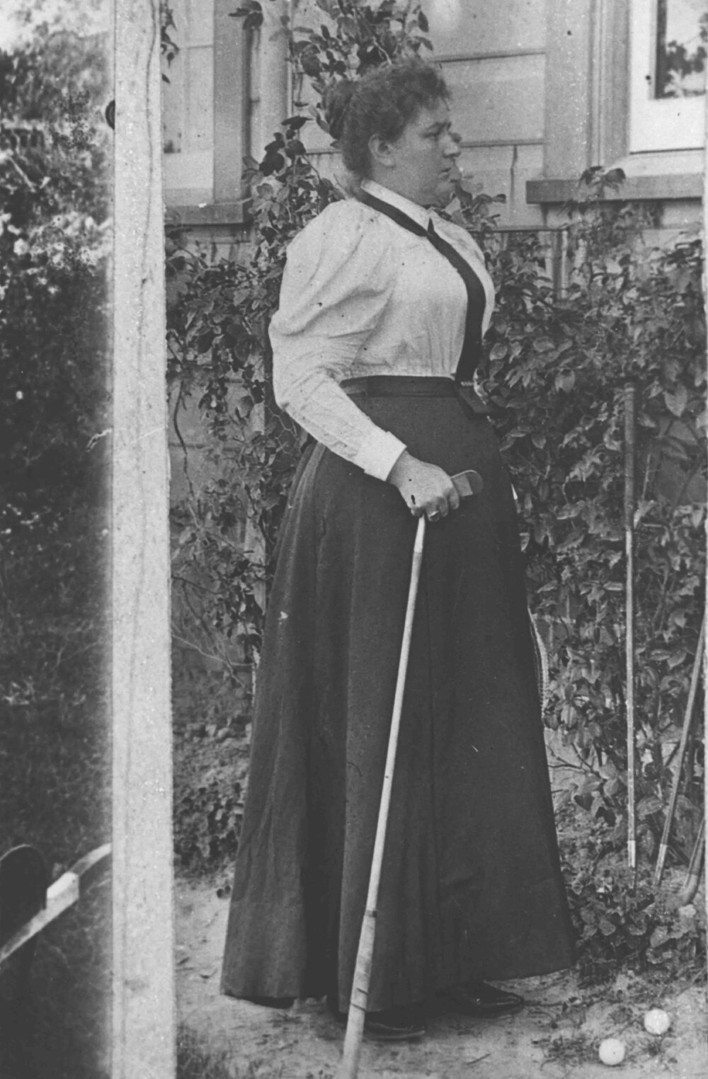 Portrait: Mrs JJ McCue - standing outside a residence holding a golf iron with two golf balls at her feet [Hawkesbury Agricultural College (HAC)]