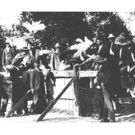 Mr McCue and students sitting on, and standing against a fence holding ostrich feathers [Hawkesbury Agricultural College (HAC)]