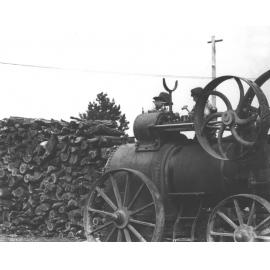 Steam traction engine next to a wood pile - two students working on the engine, one has a hammer [Hawkesbury Agricultural College (HAC)]