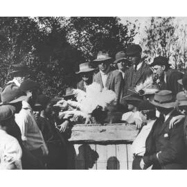 Students sitting on and standing by a fence, holding ostrich feathers [Hawkesbury Agricultural College (HAC)]
