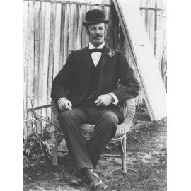 Portrait: Man, formally dressed in suit and waistcoat, wearing a bowler hat and seated in a cane chair [Hawkesbury Agricultural College (HAC)]