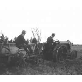 A student under instruction, driving an early tractor pulling a plough, with the instructor sitting on the plough [Hawkesbury Agricultural College (HAC)]