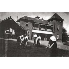 Four women, students at the University of Sydney, learning to scythe under the instruction of the gardener HW Reid. The students are scything the Fairy Circle. [Hawkesbury Agricultural College (HAC)]