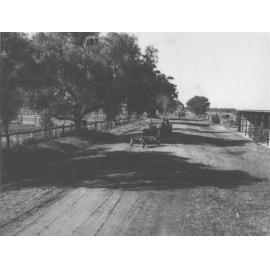 Students driving two early tractors (one pulling machinery) along a dirt road on Campus - a horse team in the background [Hawkesbury Agricultural College (HAC)]