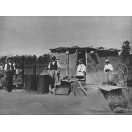 Land clearing - men standing outside a shack, around two drums with chimneys - camp kitchen? [Hawkesbury Agricultural College (HAC)]